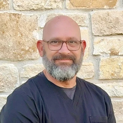 Physician Assistant MAJ (Ret.) James S. Lorenz smiling in front of a stone wall.